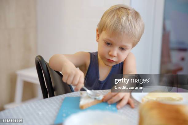toddler sitting at breakfast table and spreading butter on sliced bread by himself - sliced bread stock pictures, royalty-free photos & images