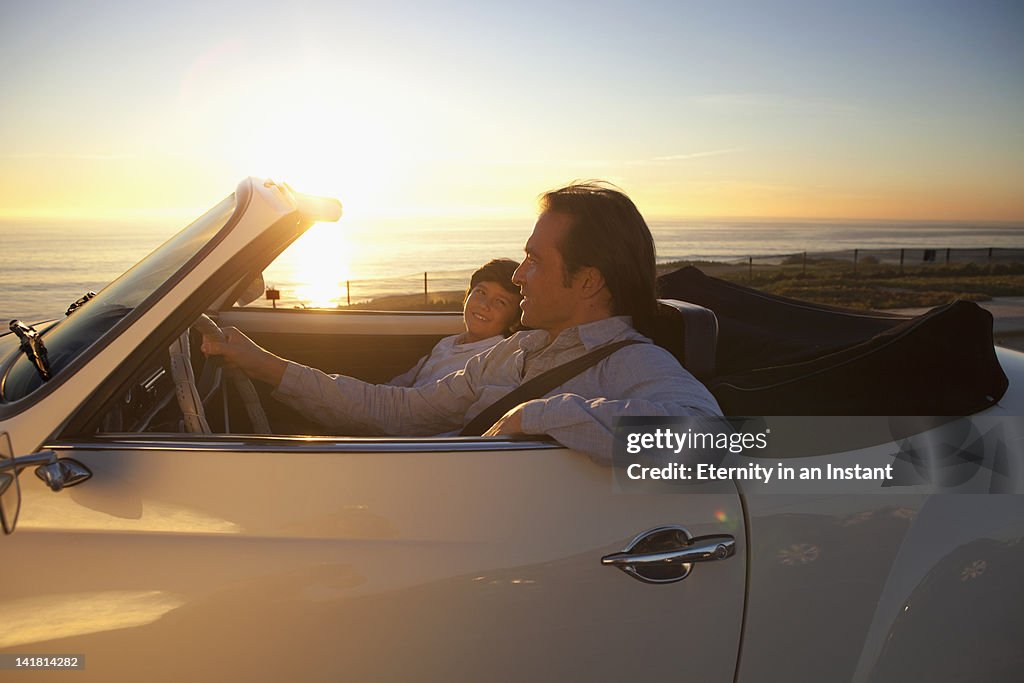 Father and son driving by ocean in convertible car