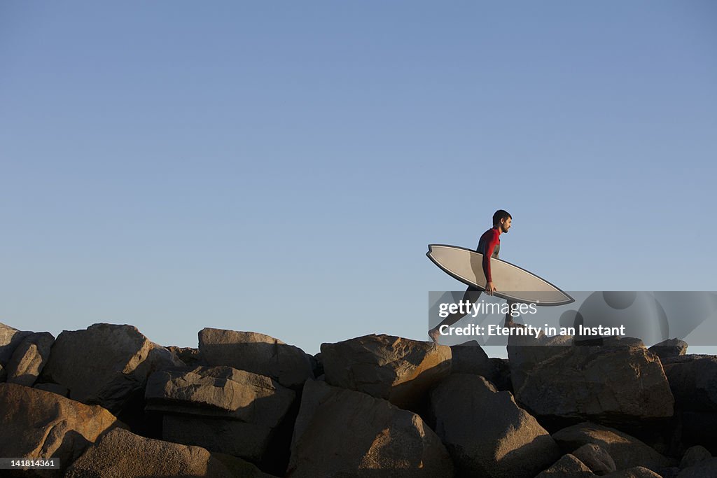 Young man with surfboard walking over rocks
