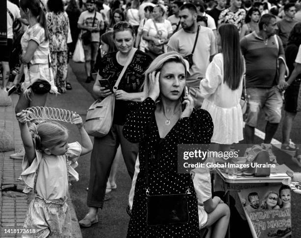 Woman call phone amid people that walk Khreshchatyk Street looking at the remains of Russian military equipment exhibited on August 21, 2022 in Kyiv,...