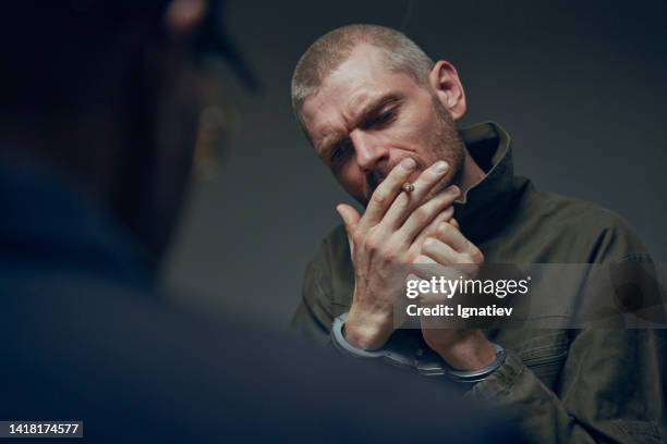 nahaufnahme eines gefangenen, der sich eine zigarette anzündet, sitzender säugling eines beamten in einem dunklen verhörraum - vernehmung stock-fotos und bilder