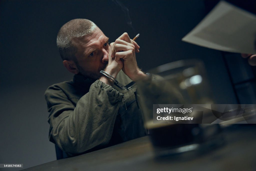 A prisoner in an interrogation room and a cup of coffee on a defocused foreground