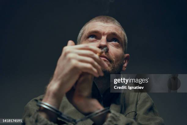 close-up of a prisoner with cigarette in handcuffs looking up on a dark background - drug dealer stock pictures, royalty-free photos & images