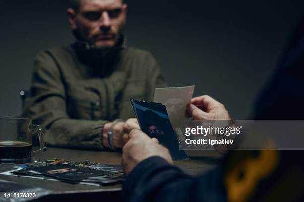a criminal in handcuffs in front of a fbi agent in a dark interrogation room - criminal offense stock pictures, royalty-free photos & images