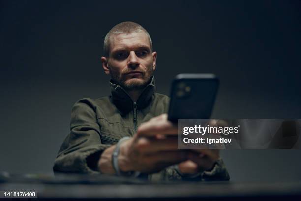 a prisoner on a dark gray background with a smartphone in his hands in handcuffs - 911 cellphone stockfoto's en -beelden