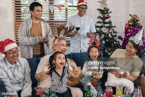 senior and grandchild group of family having fun celebrate christmas and new years party at home - asian child with new glasses stockfoto's en -beelden