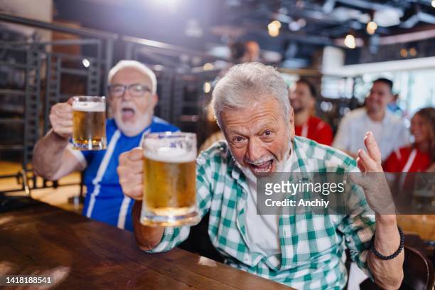excited senior men watching sports game in the pub and celebrating goal of their team - baby boomer millennial stock pictures, royalty-free photos & images