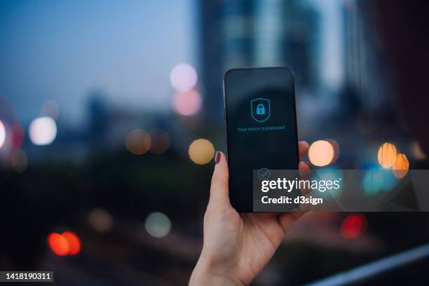 close up of female hand holding up smartphone against illuminated cityscape in the city, with security key lock icon on the device screen. privacy protection, internet and mobile security concept - digital crime stock pictures, royalty-free photos & images