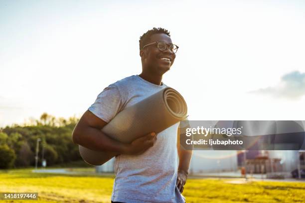 african american man holding yoga mat smiling on sunny day. - yoga outdoor stockfoto's en -beelden