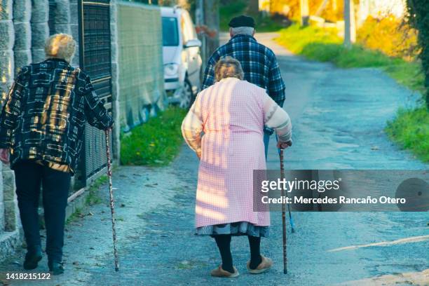 three senior people walking along the street sidewalk. - grandma cane stock pictures, royalty-free photos & images