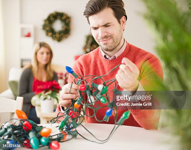 man trying to untangle christmas lights - tangled christmas lights stock-fotos und bilder