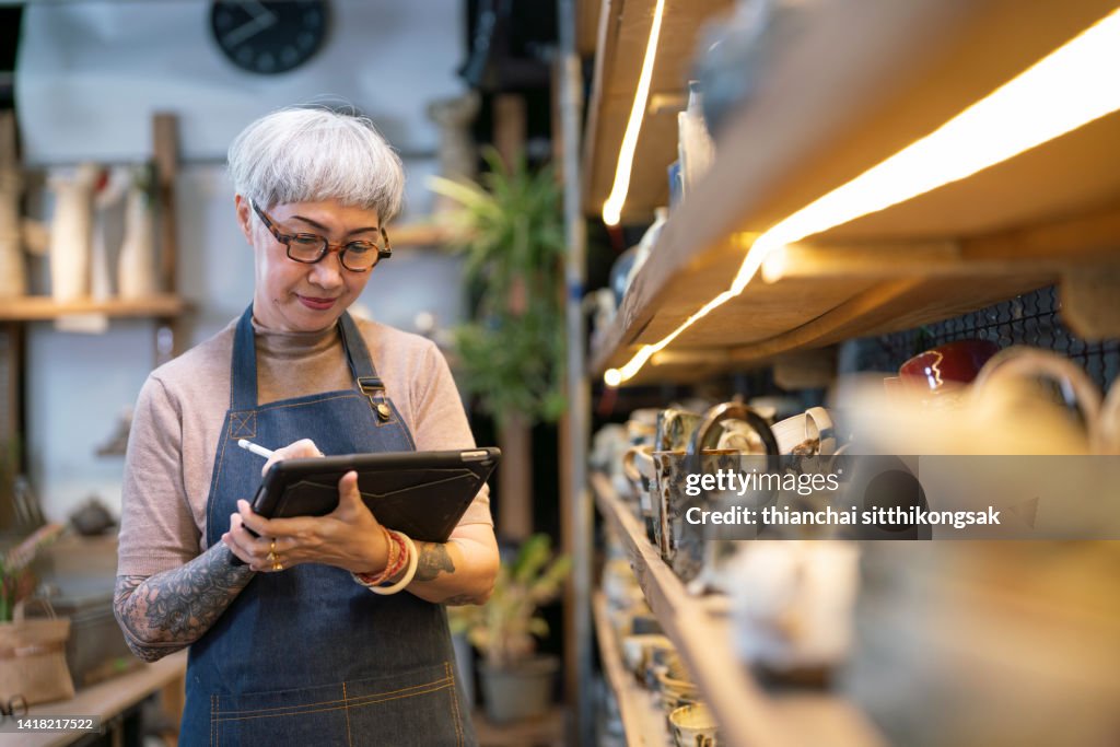Female potter using a digital tablet examining pottery in her studio.