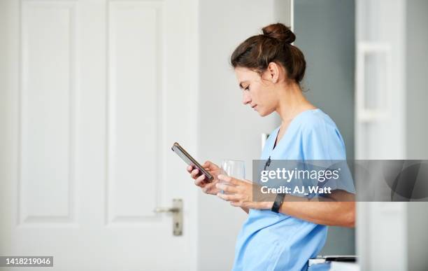 giovane infermiera con un bicchiere d'acqua usando il telefono cellulare in ospedale - infermiera foto e immagini stock