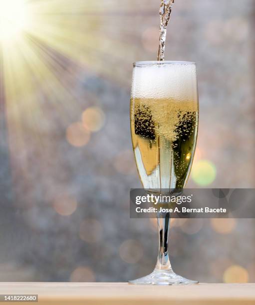 close-up fill a glass of champagne glass illuminated by sunlight. - champagnekleurig stockfoto's en -beelden