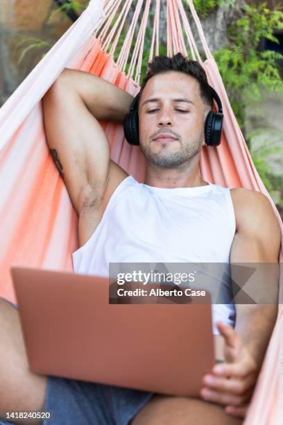 man listening to music and using the computer while lying in a hammock - young man listening music and relaxing in hammock stock pictures, royalty-free photos & images