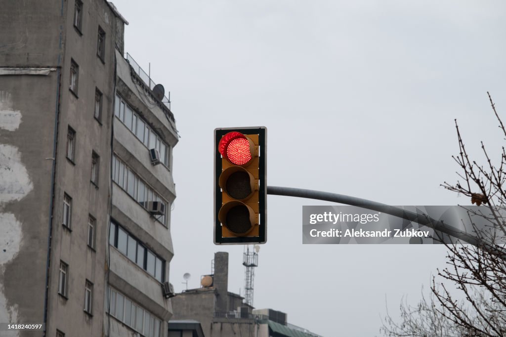 Traffic light close-up with a red signal. Traffic light on the background of a residential multi-storey high-rise building, in an old residential area. Traffic rules. Prohibited traffic light signal.