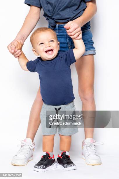 happy baby boy being helped to stand by big sister - kid in big shoes stock pictures, royalty-free photos & images