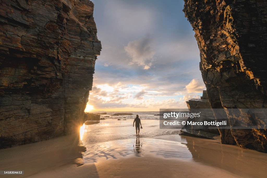 Person with a camera in Playa das Catedrais at sunset, Spain