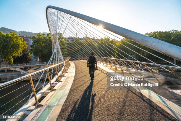 person walking under zubizuri footbridge across nervion river - bilbao stock pictures, royalty-free photos & images