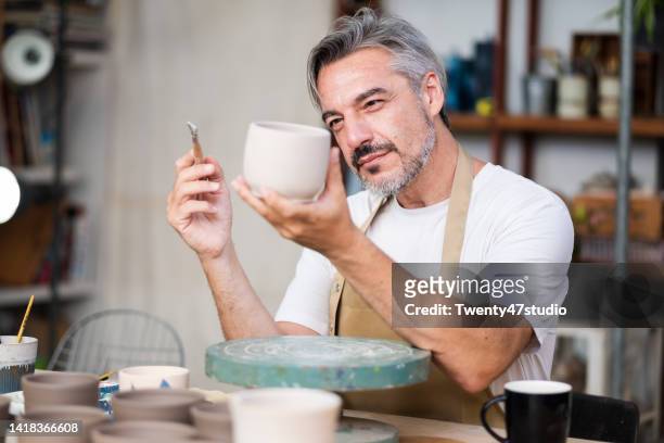 caucasian potter artist painting a ceramic cup in the pottery studio - sculptor stock-fotos und bilder