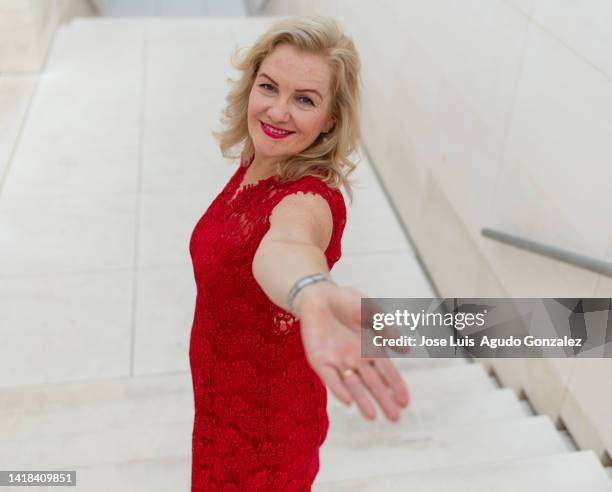 profile view of a woman in a red dress walking on some stairs inviting you with her hand. attractive older woman in a dress on some stairs inviting you to come with her hand - beckoning stock pictures, royalty-free photos & images