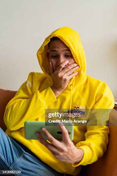ecuadorian man watches his world cup match from his cell phone while at home wearing the team's jersey - football phone stock pictures, royalty-free photos & images