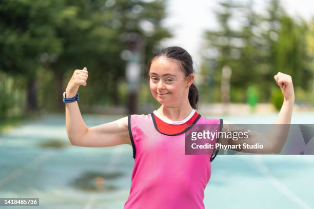 young female athlete with down syndrome posing at sport track and flexing muscles - paralympics track stock pictures, royalty-free photos & images
