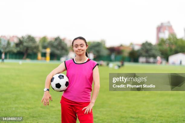portrait of young female soccer player with down syndrome posing at sport field and flexing muscles - down syndrome athlete stock pictures, royalty-free photos & images
