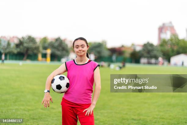 portrait of young female soccer player with down syndrome posing at sport field and flexing muscles - disabled athlete stock pictures, royalty-free photos & images