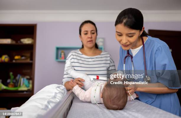 doctor making a house call visit and checking on a baby girl wearing a hip dysplasia brace - heup stockfoto's en -beelden
