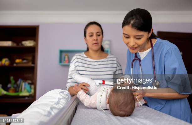 doctor making a house call visit and checking on a baby girl wearing a hip dysplasia brace - nurse with baby stock pictures, royalty-free photos & images