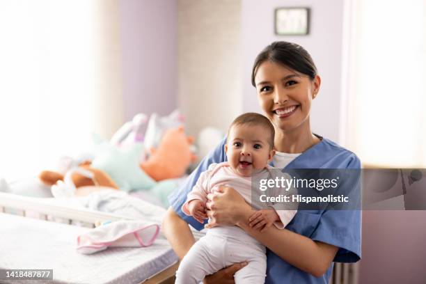 feliz enfermera cargando a un bebé en la guardería - au pair fotografías e imágenes de stock