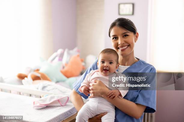 happy nurse carrying a baby in the nursery - baby sitter stock pictures, royalty-free photos & images