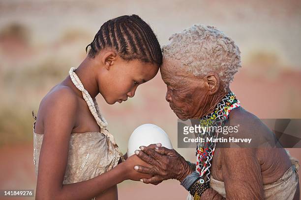 indigenous bushman/san girl given ostrich egg by grandmother (14years old, 75 years old), namibia (image taken to raise awareness and funds for the conservation pr - 14 15 years fotografías e imágenes de stock
