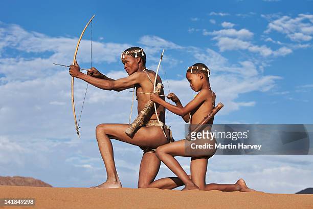 indigenous bushman/san father passing down traditional hunting techniques to his son (10 years old, 43 years old), namibia (image taken to - bushmen ストックフォトと画像
