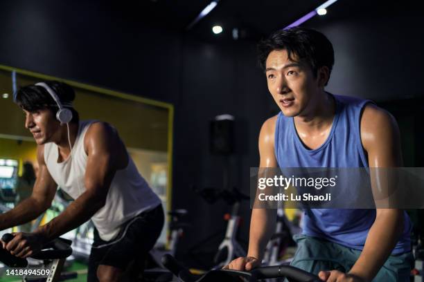 young people riding stationary bike during indoor cycling class in gym. - stationary cycling class stock pictures, royalty-free photos & images