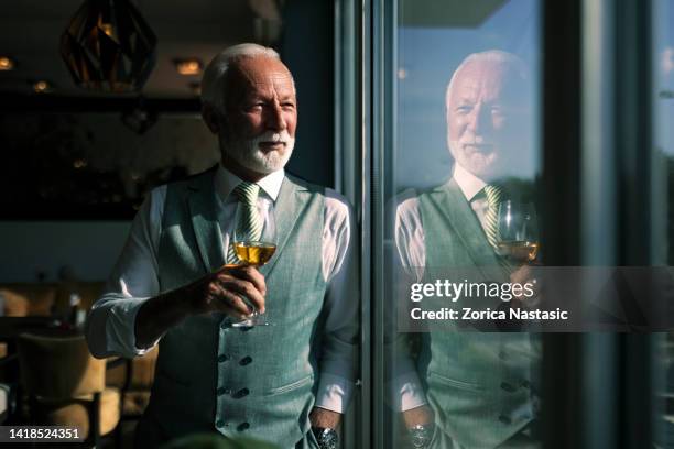 senior businessman drinking wine in a restaurant standing next to window - gentlemens club stock pictures, royalty-free photos & images