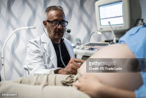 ginecologo che controlla la donna incinta con lo stetoscopio nel suo ufficio - obstetrician foto e immagini stock