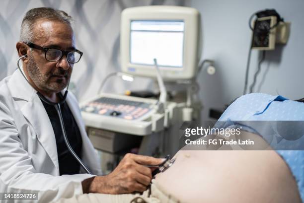 gynecologist checking pregnant woman with stethoscope at his office - auscultation woman stockfoto's en -beelden