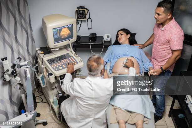 obstetrician using ultrasound scanner on pregnant mid adult woman in his office at the hospital - mexican and white baby stock pictures, royalty-free photos & images