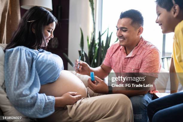 father and son painting pregnant mother's belly at the living room - surrogacy stock pictures, royalty-free photos & images