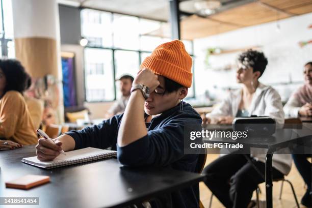 tired young man taking notes during class in the university - college student holding books stockfoto's en -beelden