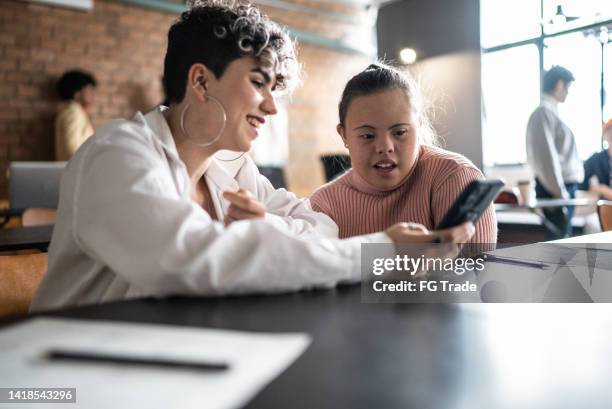 kollegen, die im klassenzimmer sprechen und smartphones nutzen - auch frauen mit besonderen bedürfnissen - developmental disability stock-fotos und bilder