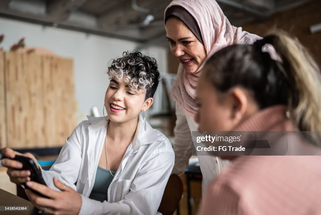 Lehrerin spricht mit Schülern im Klassenzimmer über Mobiltelefon - auch Frauen mit besonderen Bedürfnissen