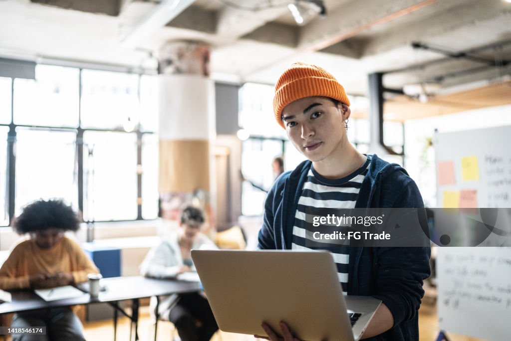 Porträt eines jungen Mannes, der den Laptop im Klassenzimmer oder in einem kleinen Unternehmen hält