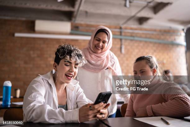 teacher and students using mobile phone in the classroom - including woman with special needs - hijab student stock pictures, royalty-free photos & images