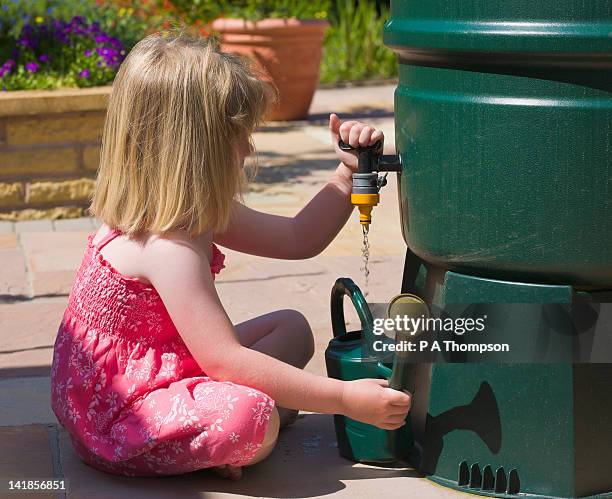 young girl collecting water in a watering can from a water butt mr pr - rainwater tank stock pictures, royalty-free photos & images