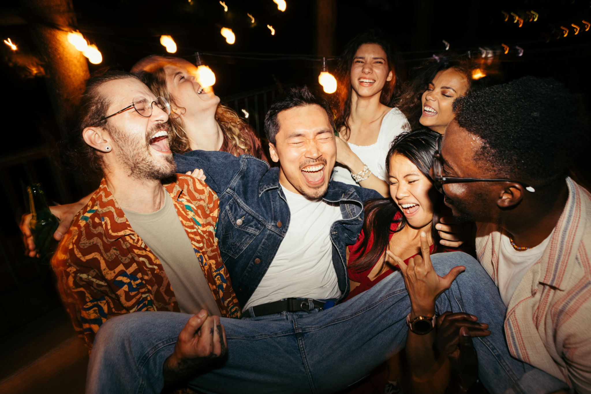 Friends lift their male friend at the night open-air rooftop party. Friends lift their male friend at the night open-air rooftop party.