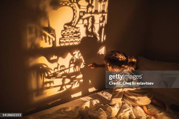 cute baby looks at the wall with shadow theatre at night before bedtime. illuminated fairytale. time to sleep - fairy tale fotografías e imágenes de stock