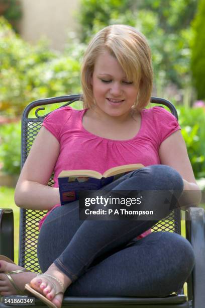 teenage girl sitting in a garden reading a book, england - girls in leggings stock-fotos und bilder